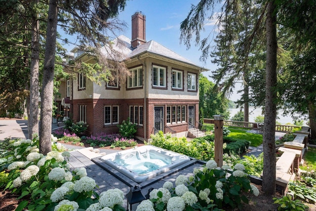 rear view of house with stucco siding, brick siding, hot tub deck surround, and a chimney