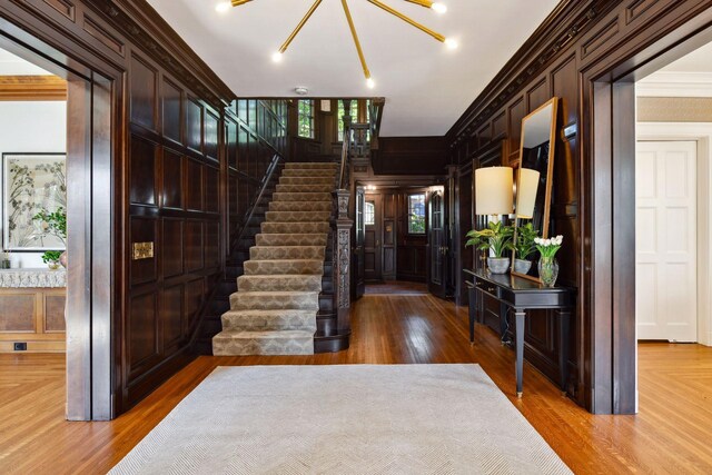 entryway featuring stairway, wood finished floors, ornamental molding, and wooden walls