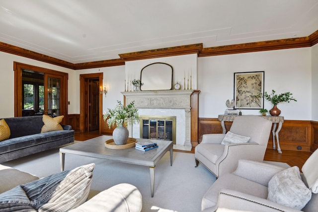 living room featuring ornamental molding, wood walls, a high end fireplace, and a wainscoted wall