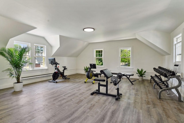 exercise area featuring lofted ceiling, a baseboard heating unit, baseboards, and wood finished floors
