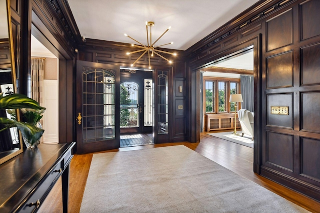 foyer featuring french doors, hardwood / wood-style flooring, crown molding, an inviting chandelier, and wood walls