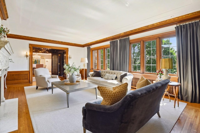 living area with ornamental molding, a chandelier, wood-type flooring, and a wainscoted wall