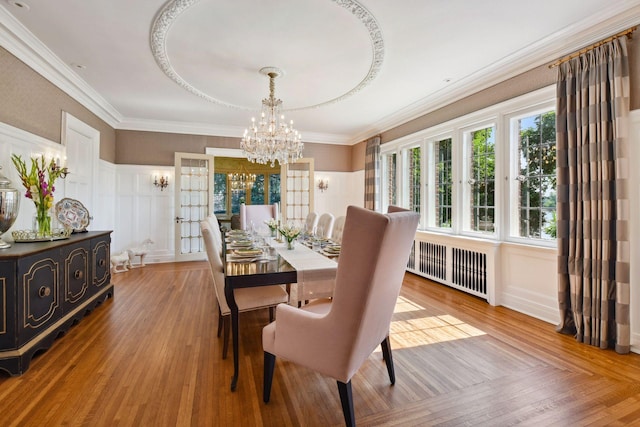 dining area with hardwood / wood-style flooring, ornamental molding, radiator heating unit, and a chandelier