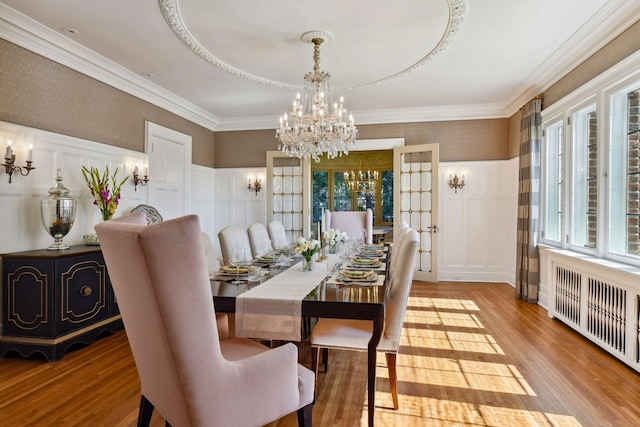 dining space featuring a tray ceiling, ornamental molding, a chandelier, radiator heating unit, and light hardwood / wood-style floors