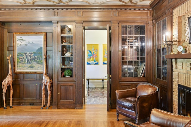 interior space with light hardwood / wood-style floors, wood walls, ornamental molding, and a brick fireplace