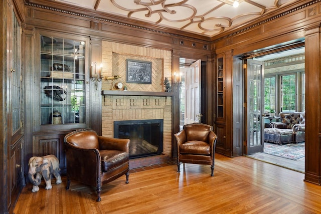 sitting room featuring a brick fireplace, wood walls, wood finished floors, and ornamental molding