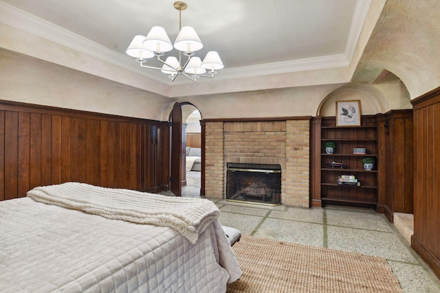 bedroom featuring light speckled floor, crown molding, a brick fireplace, arched walkways, and a notable chandelier
