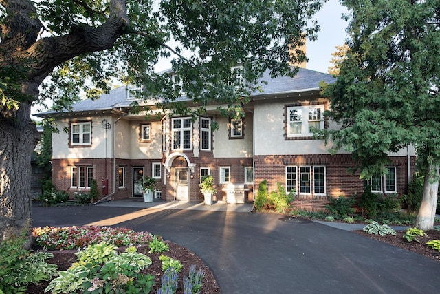 view of front facade with driveway, stucco siding, and brick siding