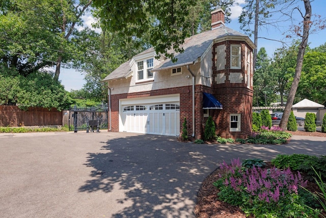 view of front of house featuring fence, brick siding, driveway, a garage, and a chimney