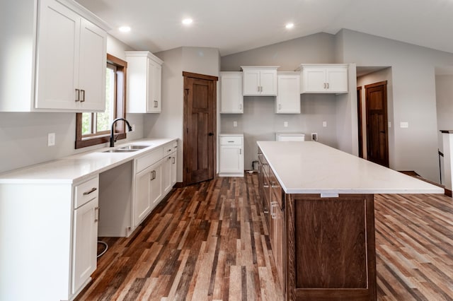 kitchen featuring white cabinets, vaulted ceiling, sink, a center island, and dark wood-type flooring