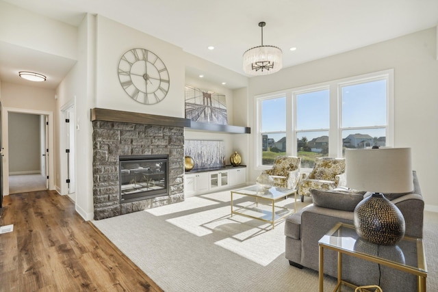 living room featuring hardwood / wood-style floors, a notable chandelier, and a stone fireplace