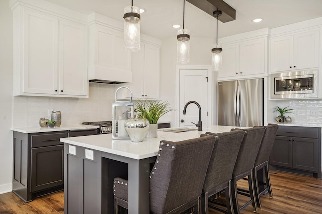 kitchen featuring a kitchen island with sink, stainless steel appliances, hanging light fixtures, dark hardwood / wood-style flooring, and sink