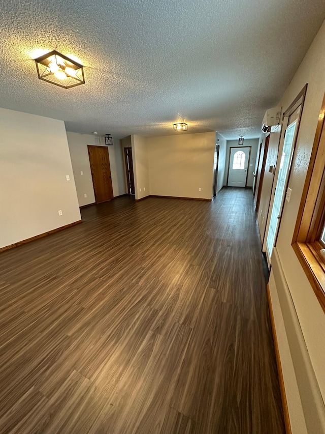 empty room with a textured ceiling, a wall mounted AC, and dark wood-type flooring