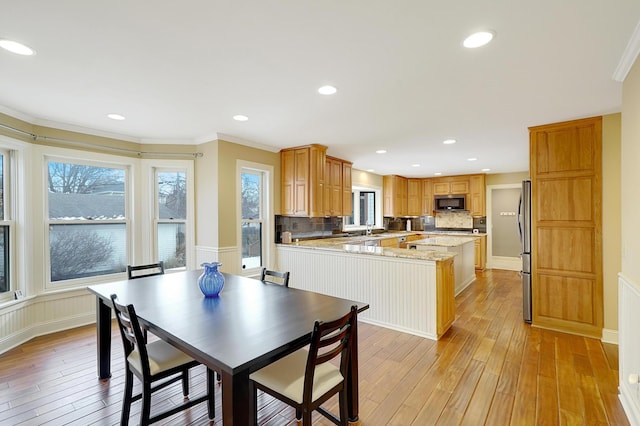 kitchen featuring stainless steel refrigerator, light wood-type flooring, crown molding, and light stone countertops