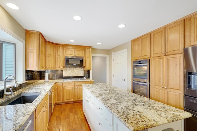 kitchen with appliances with stainless steel finishes, sink, light hardwood / wood-style flooring, and light stone countertops