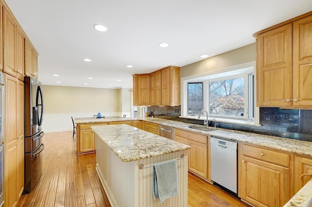 kitchen with sink, a center island, light hardwood / wood-style floors, light stone countertops, and appliances with stainless steel finishes