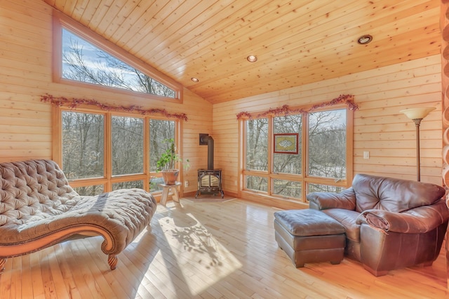 interior space featuring a wood stove, high vaulted ceiling, wooden walls, wood ceiling, and light wood-type flooring