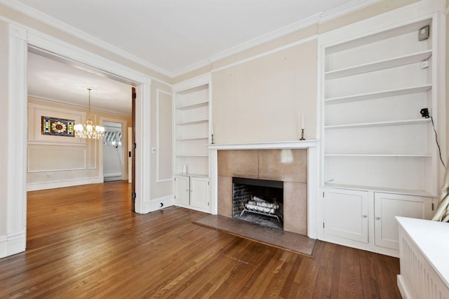 unfurnished living room with built in shelves, an inviting chandelier, a tiled fireplace, and crown molding