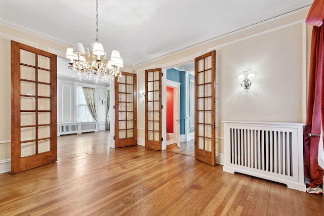 spare room featuring hardwood / wood-style floors, crown molding, french doors, radiator heating unit, and an inviting chandelier