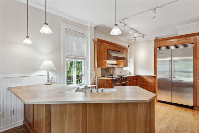 kitchen featuring kitchen peninsula, pendant lighting, premium appliances, wall chimney range hood, and crown molding