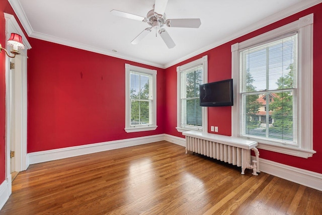 empty room featuring a healthy amount of sunlight, hardwood / wood-style floors, ornamental molding, and radiator