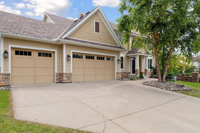 craftsman-style house with a garage, stone siding, roof with shingles, and driveway