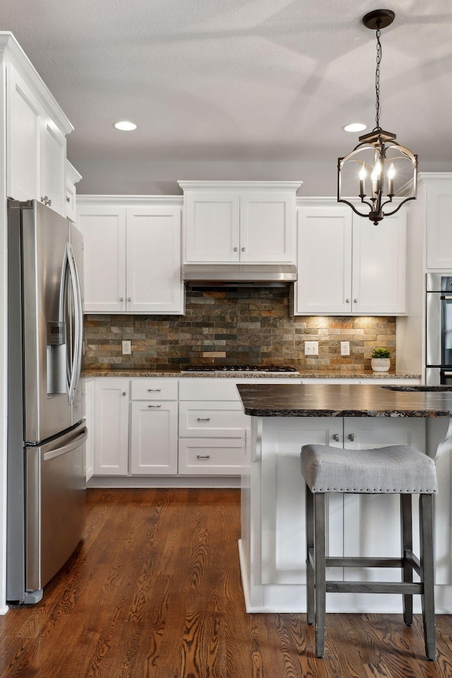 kitchen with pendant lighting, tasteful backsplash, appliances with stainless steel finishes, white cabinetry, and under cabinet range hood