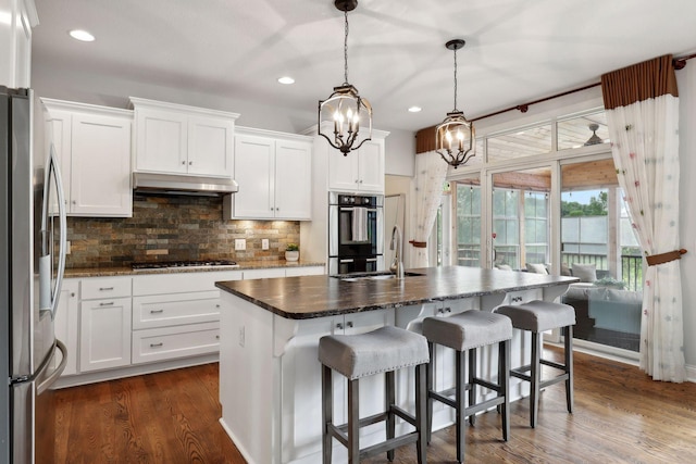 kitchen with white cabinets, a sink, a center island with sink, and under cabinet range hood