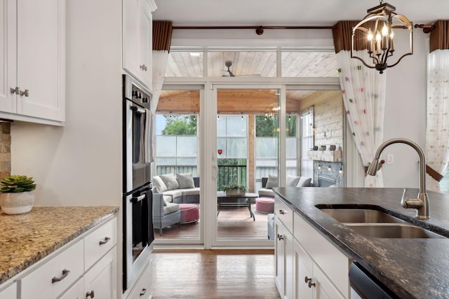 kitchen featuring white cabinets, light wood-style flooring, appliances with stainless steel finishes, dark stone countertops, and a sink