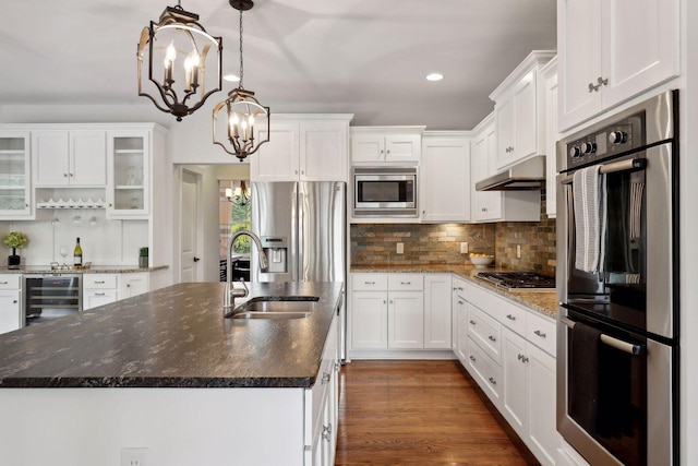 kitchen with a center island with sink, glass insert cabinets, appliances with stainless steel finishes, white cabinetry, and under cabinet range hood