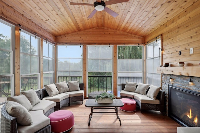 sunroom featuring vaulted ceiling, ceiling fan, a stone fireplace, and wooden ceiling