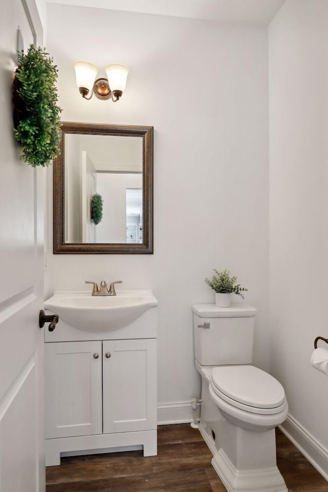 half bathroom featuring baseboards, vanity, toilet, and wood finished floors