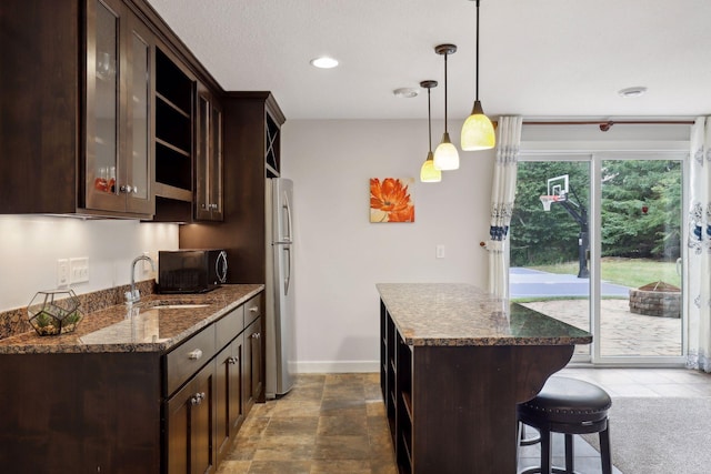 kitchen with pendant lighting, dark brown cabinetry, a sink, dark stone counters, and black microwave