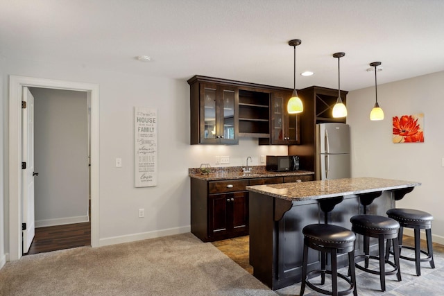 kitchen with black microwave, stone counters, dark brown cabinetry, freestanding refrigerator, and glass insert cabinets