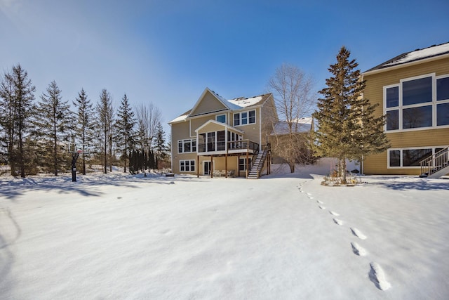 snow covered house with stairs, a deck, and a sunroom