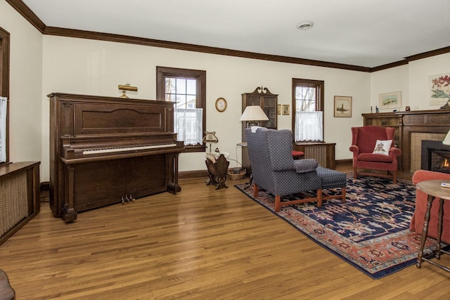 living area with plenty of natural light, light wood-style flooring, ornamental molding, and a tiled fireplace