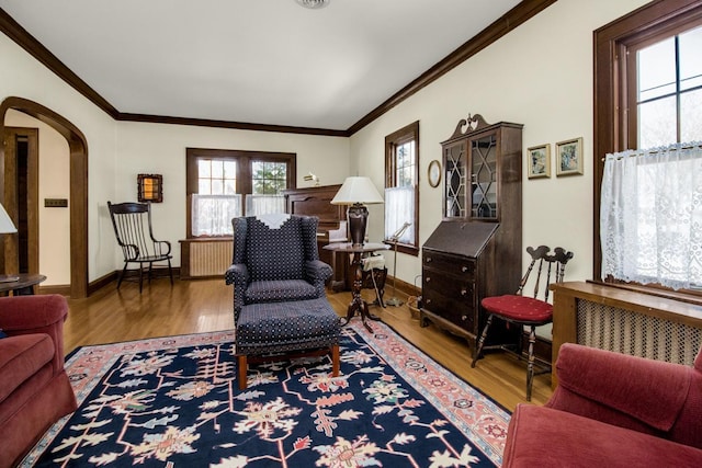 living room with arched walkways, crown molding, baseboards, and wood finished floors