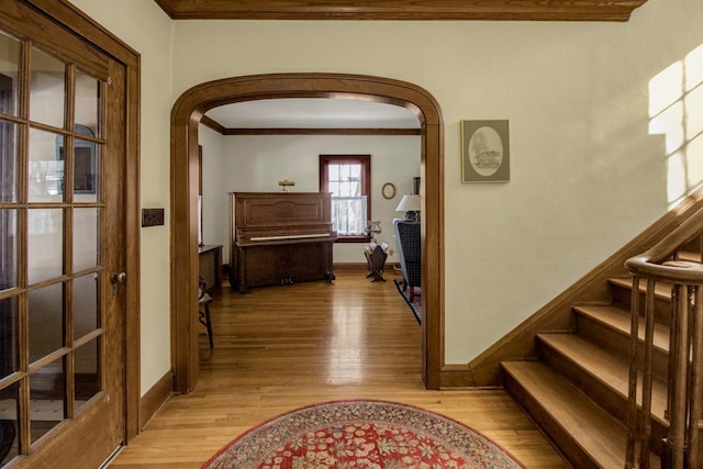 hall with arched walkways, ornamental molding, stairway, and light wood-style flooring