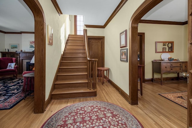 staircase with arched walkways, crown molding, baseboards, and wood finished floors