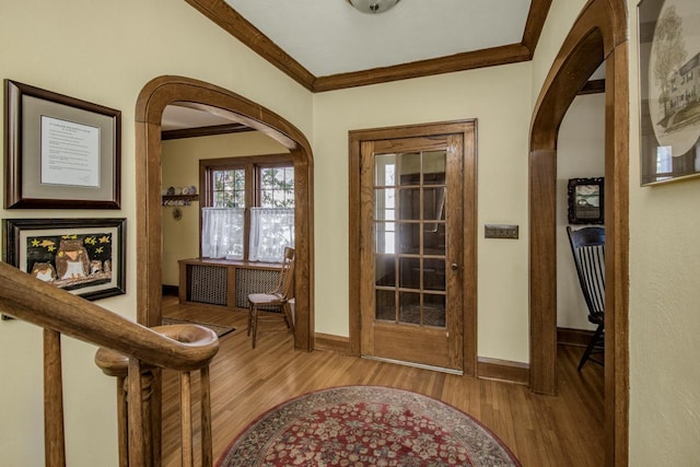 entryway with light wood-style floors, baseboards, arched walkways, and crown molding