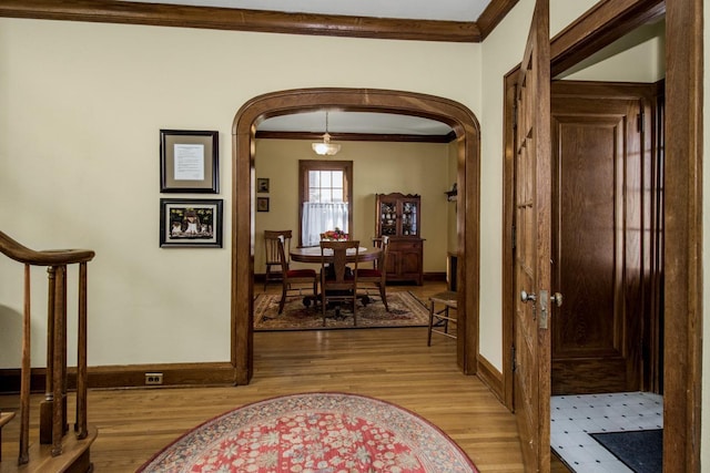 hallway with arched walkways, crown molding, light wood-style flooring, and baseboards