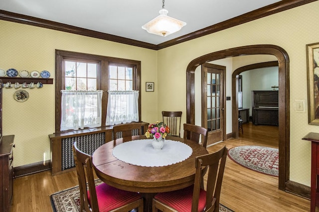 dining room with wallpapered walls, baseboards, arched walkways, ornamental molding, and wood finished floors