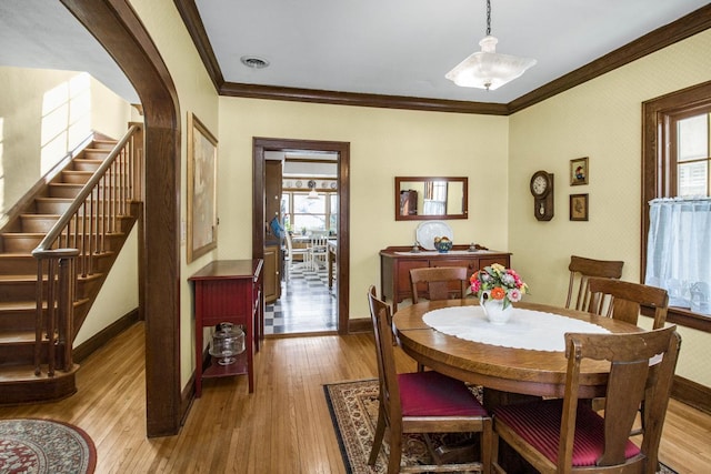 dining room featuring baseboards, arched walkways, light wood-style flooring, stairway, and crown molding