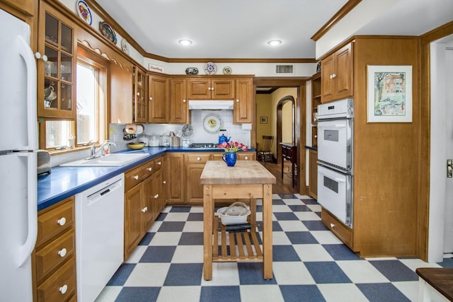 kitchen with white appliances, dark floors, brown cabinetry, and a sink