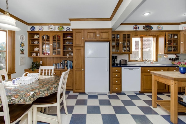 kitchen with white appliances, brown cabinetry, dark countertops, glass insert cabinets, and a sink