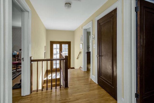 hallway with baseboards, wallpapered walls, an upstairs landing, and light wood-style floors