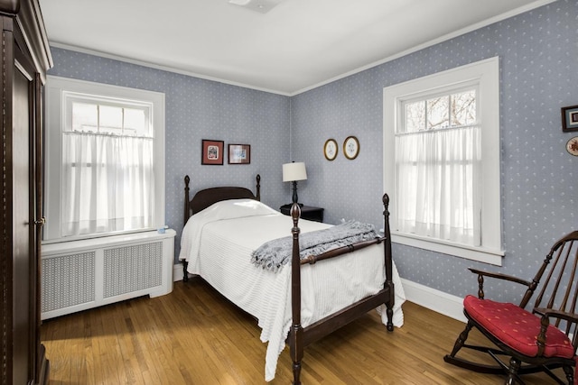 bedroom featuring wood finished floors, baseboards, ornamental molding, radiator, and wallpapered walls