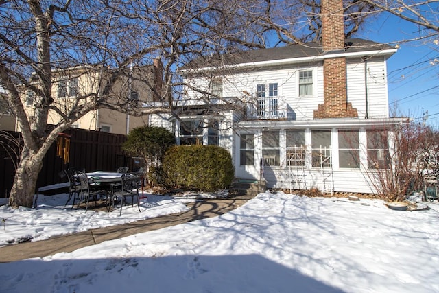 snow covered back of property with entry steps, a sunroom, fence, and a chimney