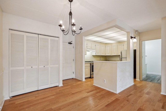 kitchen with white refrigerator, stainless steel range oven, light wood-type flooring, and hanging light fixtures