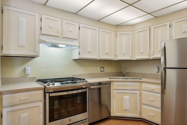 kitchen with a drop ceiling, sink, light hardwood / wood-style flooring, and appliances with stainless steel finishes